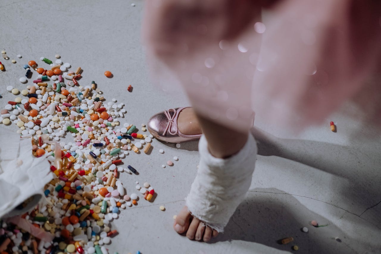 A childs foot in a cast next to a pile of scattered pills on a white floor.