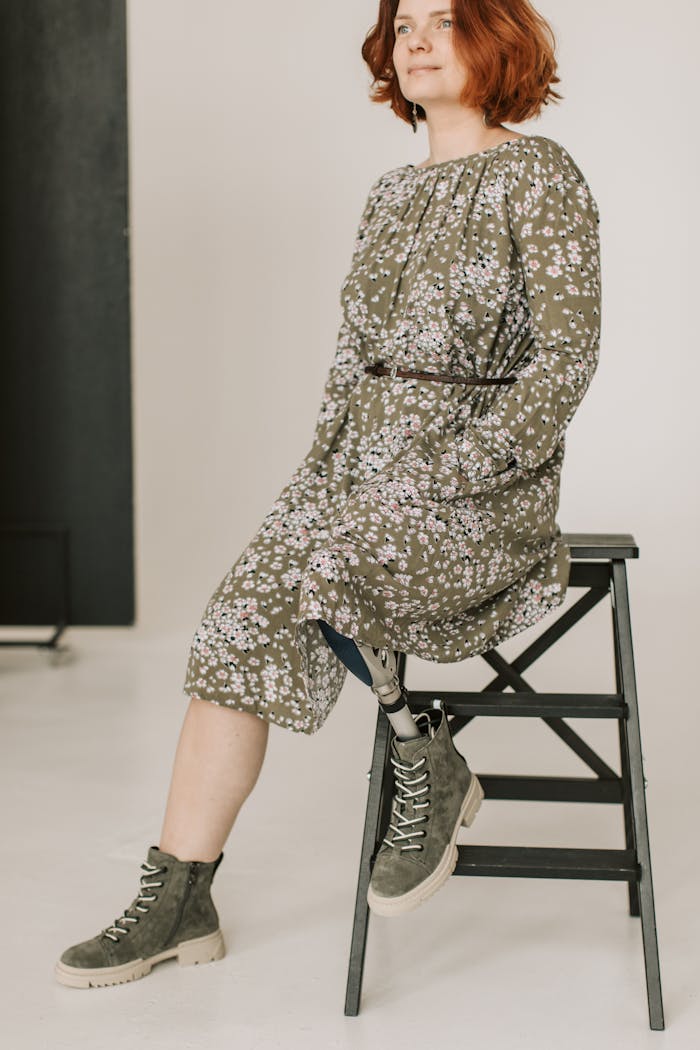 Woman with a prosthetic leg sitting confidently in floral dress on stool.