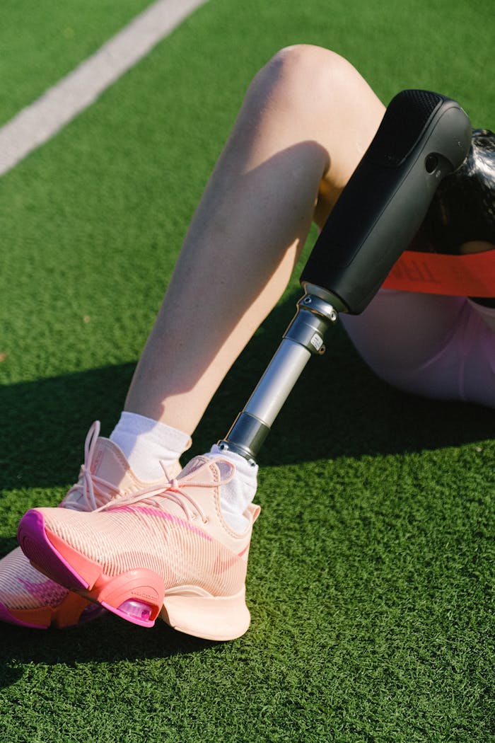 Close-up of a female athlete with a prosthetic leg resting on grass in bright sneakers.